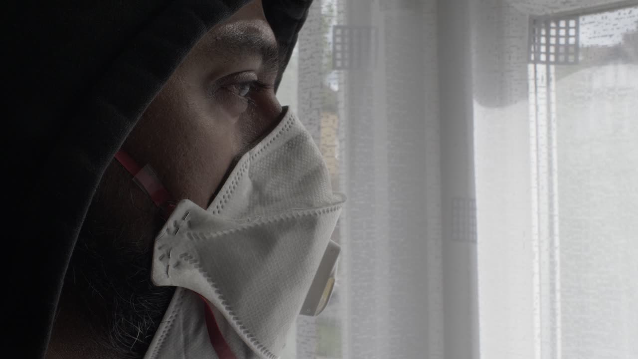 실내에서 커튼을 통해 보고 있는 ffp 3개의 마스크를 착용한 두건을 쓴 성인 아시아 남성