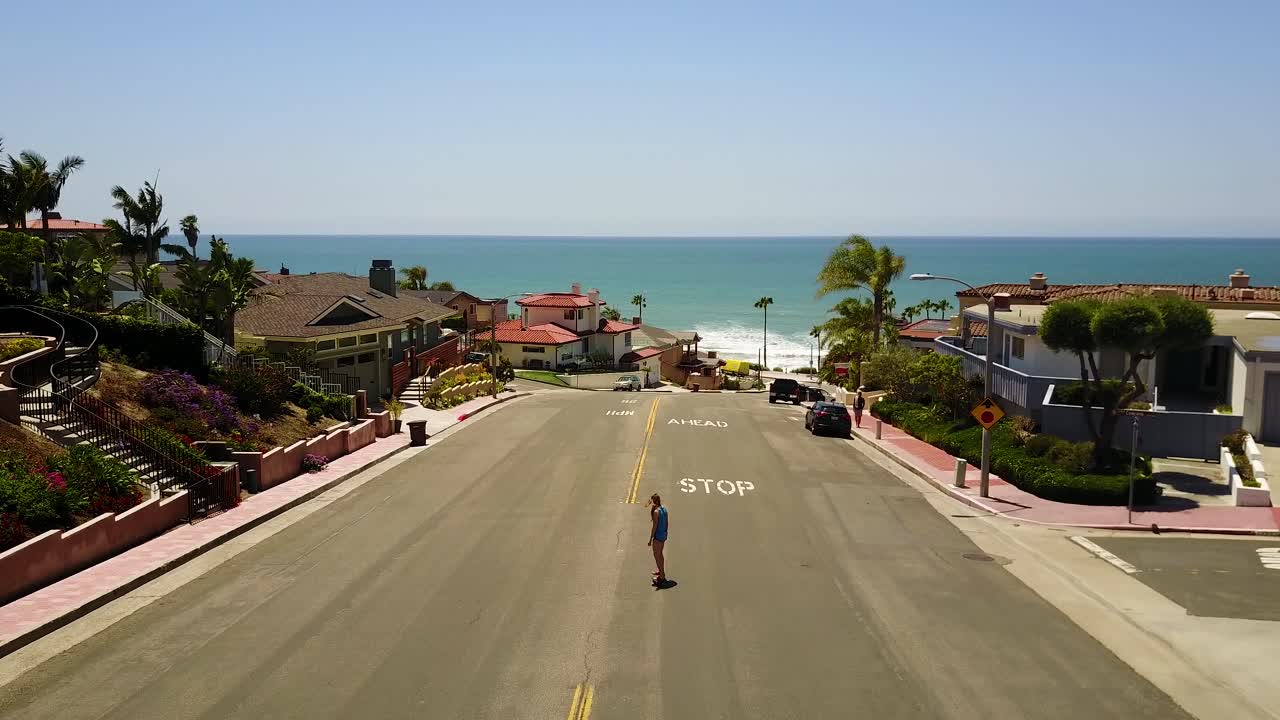 una niña montando una patineta por una pequeña colina cerca de una playa del sur de california