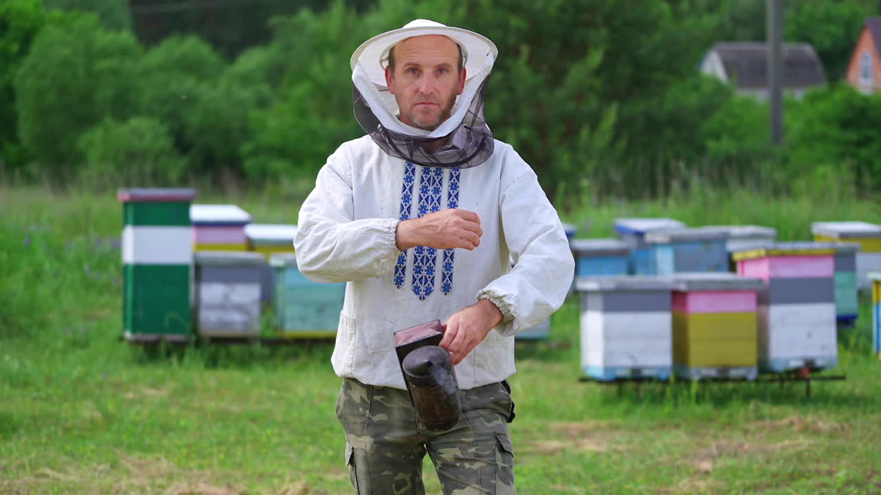 Portrait of beekeeper man. Apiarist in white shirt and protective hat holding chimney with smoke and smiling on camera. Beekeeper at the apiary.