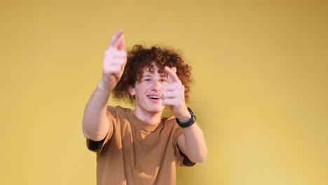 A Cheerful Playful Young Man with a Chic Hairstyle Shows Positive Emotions to the Camera a Cheerful Playful Young Man with a Chic Hairstyle Shows Positive Emotions to the Camera Hand Gestures a Student on a Brown Background