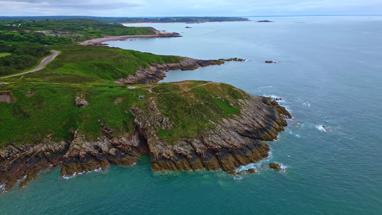 The drone pulls back while slightly ascending over Pointe aux Chèvres, revealing rocky cliffs, sea, and coastal vegetation in Brittany. France