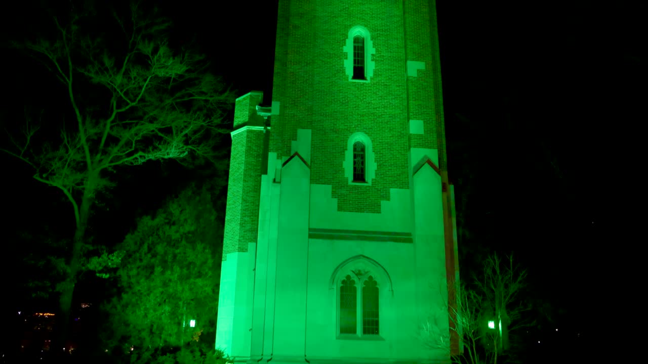 torre beaumont en el campus de la universidad estatal de michigan iluminada de noche en verde en honor a las víctimas del tiroteo masivo de febrero de 2023 con video de cierre inclinado hacia el reloj