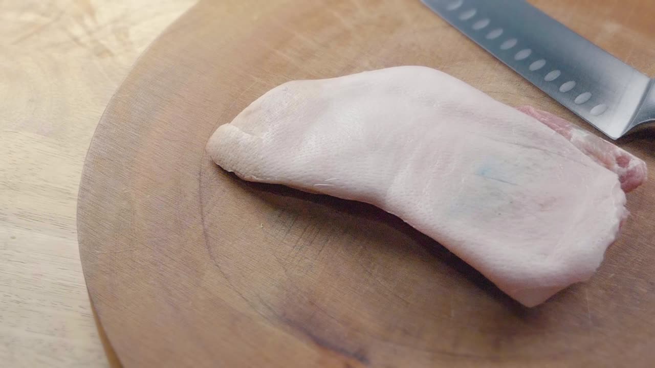 나무 도마 위에 있는 셰프의 칼 옆에 있는 신선한 익히지 않은 삼겹살의 중간 슬라이더 샷