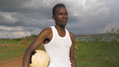 Slow-motion-orbit-shot-to-the-face-of-a-young-African-man-holding-a-football-while-looking-out-to-Lake-Victoria