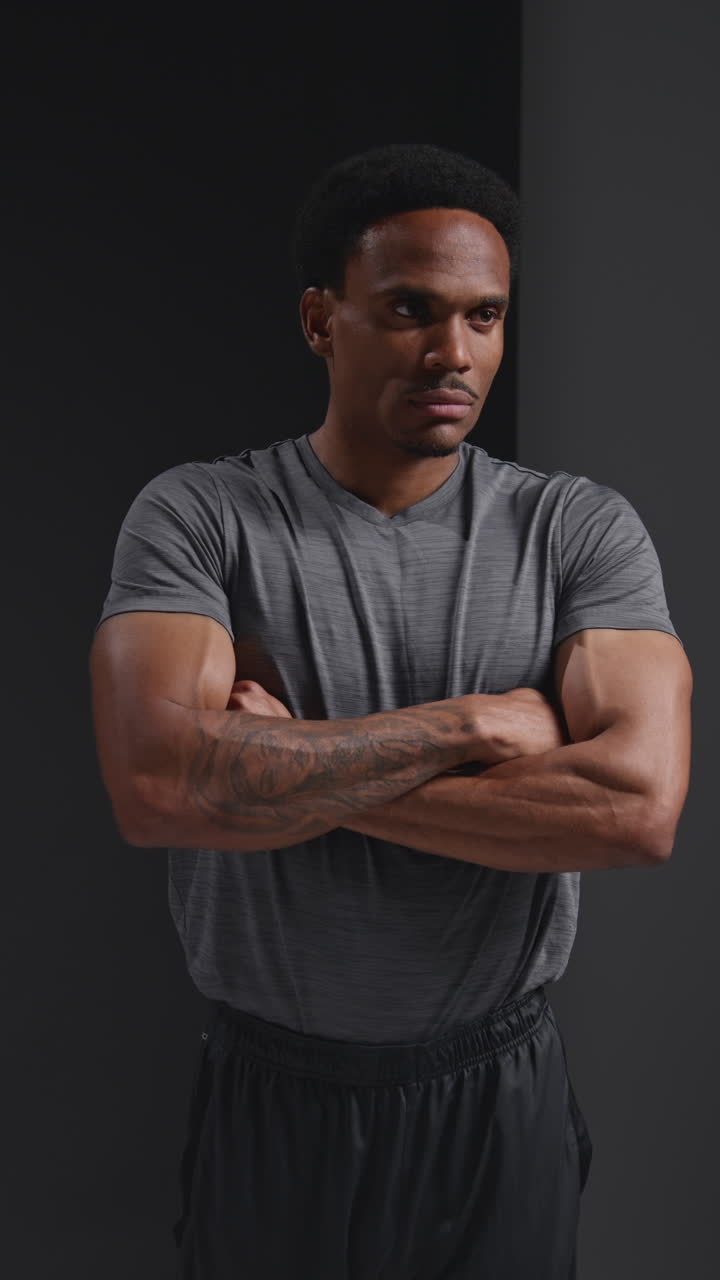 retrato vertical de estudio de video de un atleta masculino entrenando o haciendo ejercicio en el gimnasio doblando los brazos contra un fondo negro