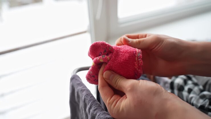 Hands pair a pink kids sock together in soft window light, sorting clean laundry at home. Cozy parenting routine, household organization, lifestyle b-roll