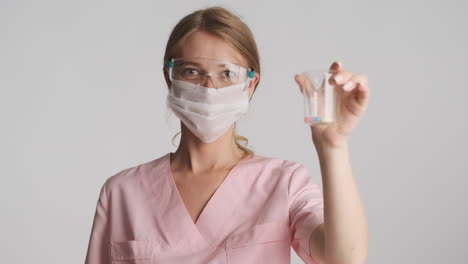 doctora caucásica con gafas de seguridad y máscara sosteniendo un frasco con pastillas.