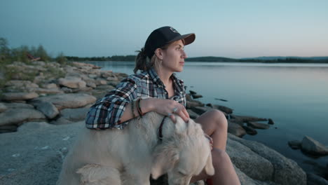 woman sitting by lake and petting dog at sunset