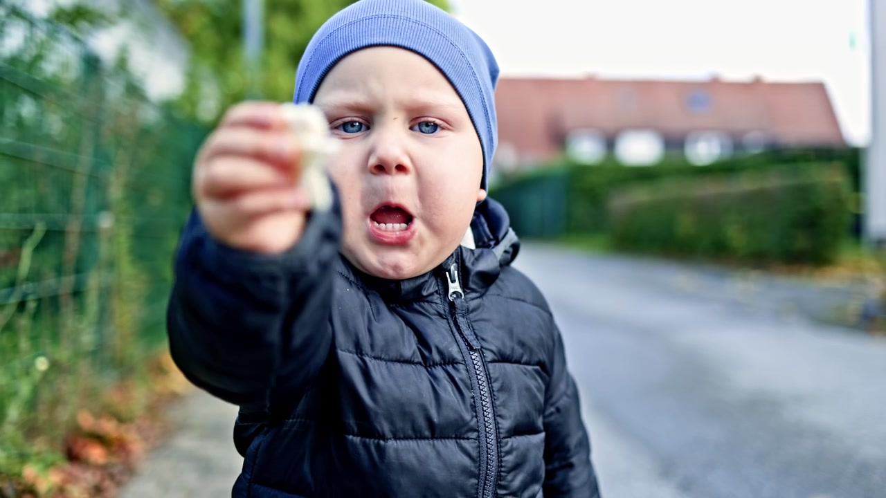 Un bambino cammina all'aperto e respira aria fresca. Un bambino piccolo, con giacca e cappello, cammina all'aperto durante una passeggiata autunnale. Un bambino mangia un panino durante una passeggiata autunnale.