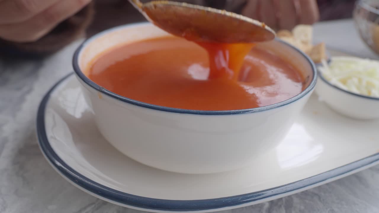 Nærbilde av en skje som rører varm tomatsuppe i en hvit bolle