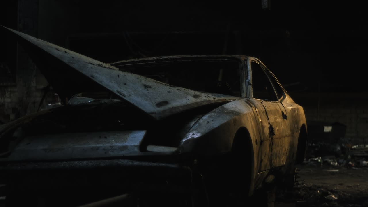 Isolated burnt car located in an abandoned warehouse. The only light of day the car sees is the sunlight beaming through the small holes in the roof of the warehouse. Blue light shining off the hood