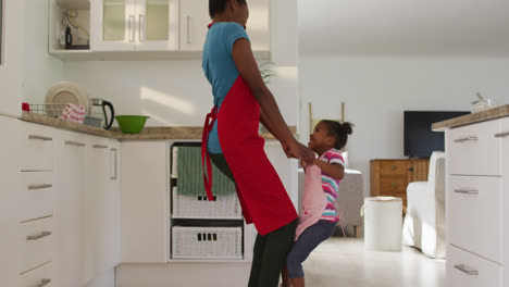 happy african american mother and daughter dancing and having fun in kitchen