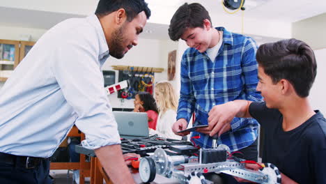 high school teacher with male pupils building robotic vehicle in science lesson