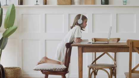 a blonde girl with headphones stares intently at the laptop screen