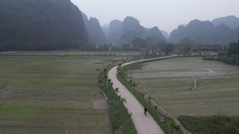 Luftaufnahme-Eines-Bikers,-Der-Durch-Das-Tal-Der-Reisfelder-Und-Klippen-In-Der-Bergregion-Von-Ninh-Ninh-Im-Norden-Vietnams-Fährt