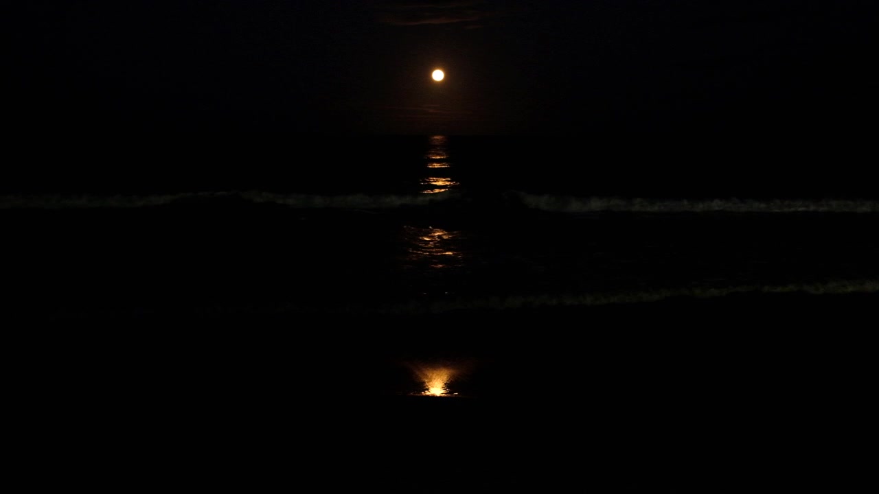 Striscia di chiaro di luna che si increspa sulla superficie dell'oceano mentre sorge la luna piena delle fragole