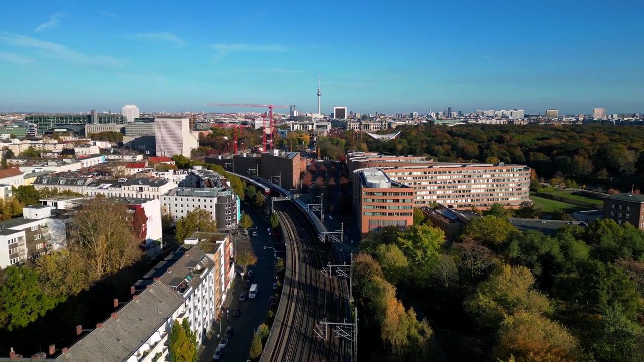 Malerische Ansicht eines Zuges, der eine Brücke über einen Fluss in Berlin überquert, umgeben von leuchtendem Herbstlaub. Majestätischer Drohnenflug mit Verfolgungsaufnahme aus der Luft.
