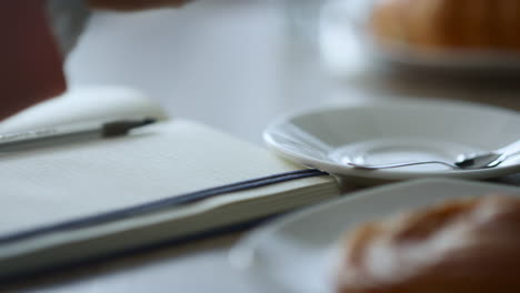 Mano-De-Mujer-Tomando-Notas-Escribiendo-Ideas-De-Negocios-En-Un-Bloc-De-Notas-Sentado-En-Una-Cafetería.