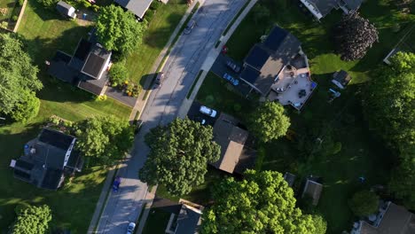 quiet charming american neighborhood with black solar panels units on roof of single family houses. green garden grass at sunset time. aerial top down rising shot. upper class residential area in usa