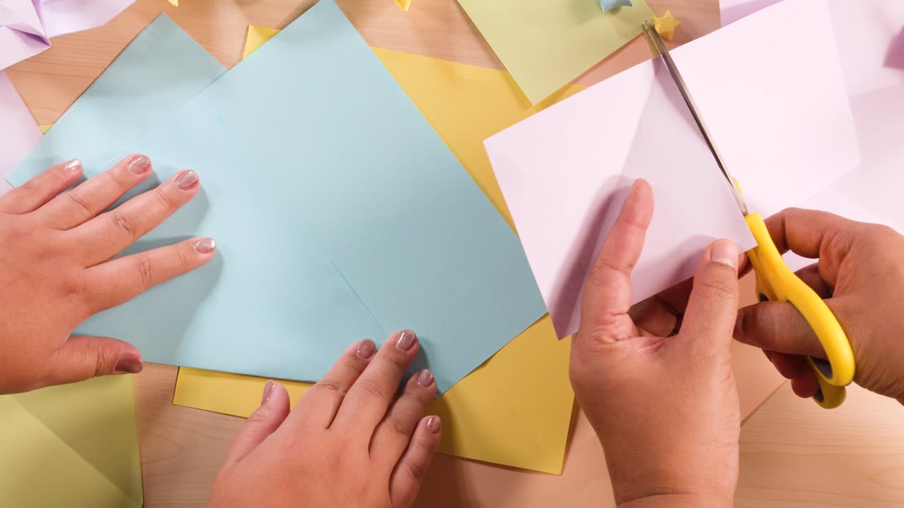 Vista dall'alto di mani che usano le forbici per tagliare e piegare la carta per l'origami