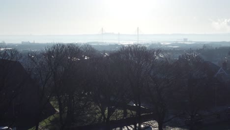 niebla helada que rodea los tejados de las casas urbanas británicas vista aérea temprano en la mañana panorámica izquierda a través de los árboles del parque