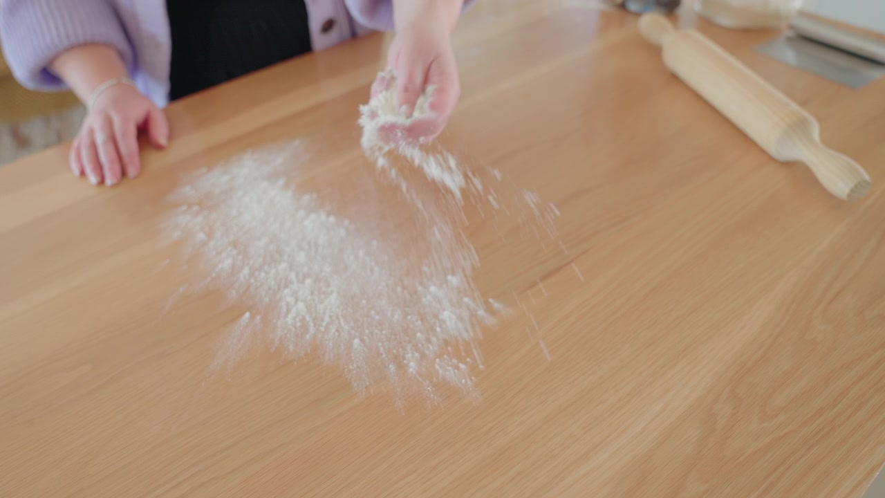 Flour spread over counter top. Dough ball being cut in a bright and open kitchen. Pizza and bread on top of counter top and flour