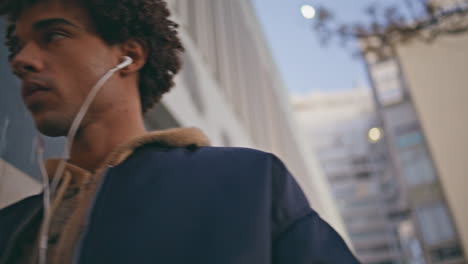 mixedrace guy listening song in earphones strolling city closeup. curly teenager