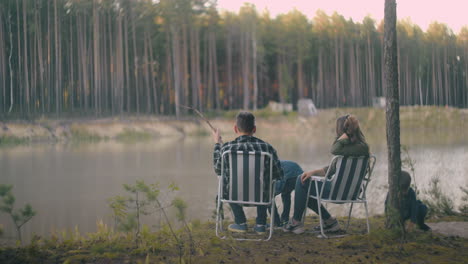 happy family is resting on coast of small forest lake at summer or fall vacation spouses and their little sons are enjoying nature