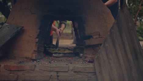 woman placing paraguayan chipa into the tatakua, a traditional handmade clay oven from paraguay