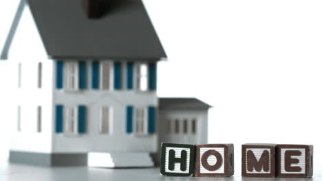 blocks spelling home sliding along in front of a miniature house