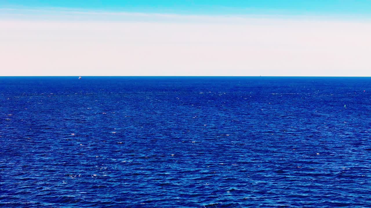 Baltic Sea Expansive, Low-Angle View Capturing the Deep, Serene Blue Waters Under a Clear, Bright Sky Transitioning from White to Light Blue at the Horizon Subtle Surface Ripples Distant Visible Boat