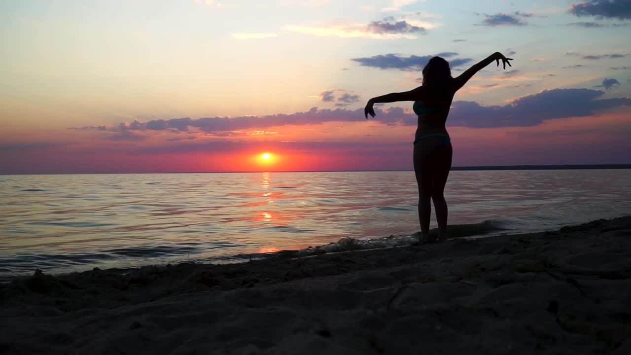 silueta bailando de una chica en traje de baño frente al mar al atardecer