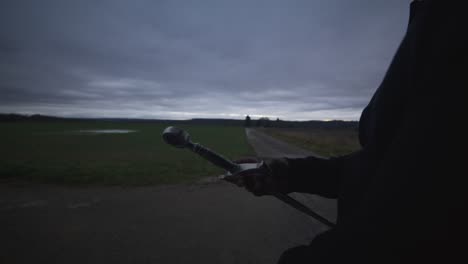 modern black swordsman warrior awaiting battle opponent in open field under grey sky, europe, 4k | muscular, intimidating, shadow, figure, blurry, dark clothes, powerful, thinking, hand