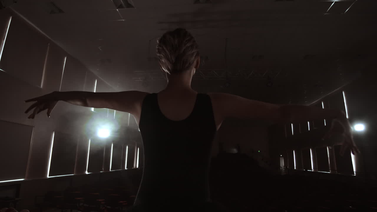 Slow motion: prima ballet on stage rehearsing performance in the dark light of the contra. The lights from the hall