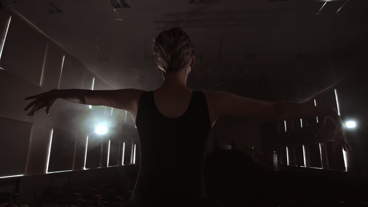 Slow motion: prima ballet on stage rehearsing performance in the dark light of the contra. The lights from the hall