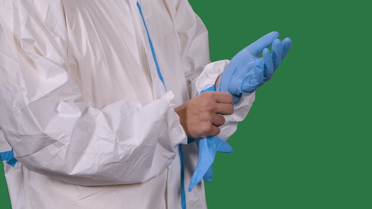 trabajador médico profesional en un traje de protección blanco se pone guantes quirúrgicos azules. torso y manos hombre de cerca. pantalla verde, llave de croma. cámara lenta