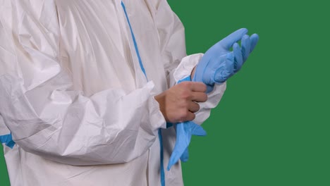 male medical worker professional in a white protective suit puts on blue surgical gloves. torso and hands man close up. green screen, chroma key. slow motion