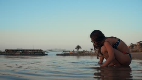 attractive teenager girl touching water at sunset coastline in evening.