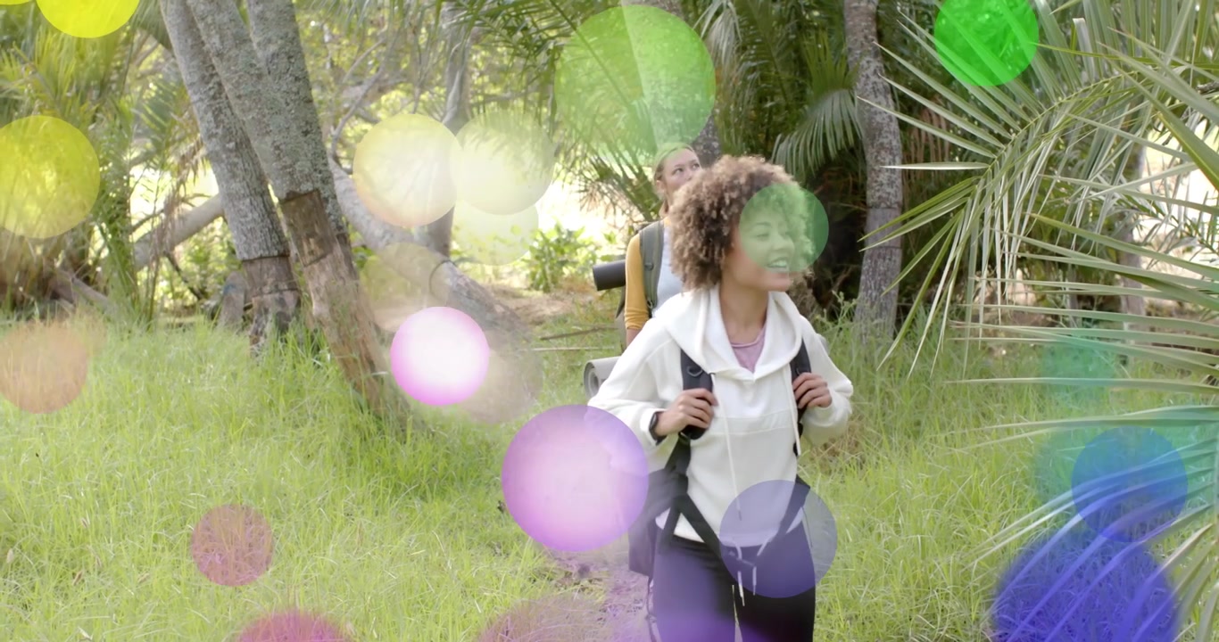 Travel two female hikers walking into palm grove exploring canopy causing colorful circles drifting