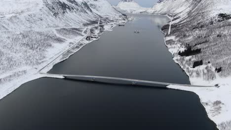 drohnenansicht im tromso-gebiet im winter über einem fjord, der von weißen bergen umgeben ist, und einer brücke in norwegen