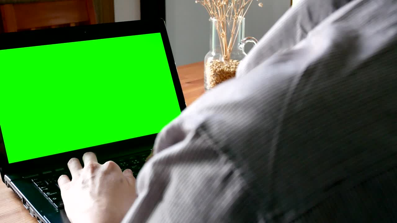 dolly shot: business man working on laptop computer with green screen for chroma key in living room - domestic indoor scene
