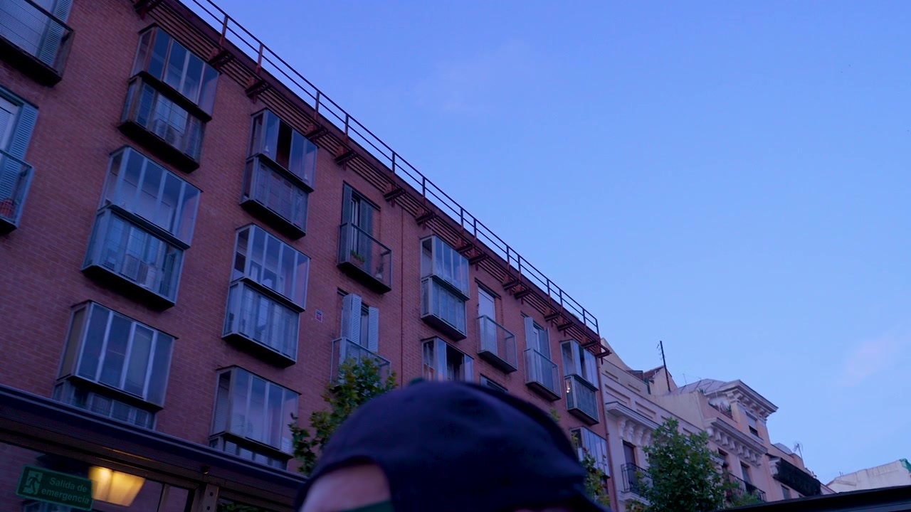Una ripresa a mano libera dal basso che cattura la facciata di edifici residenziali tradizionali e moderni a Madrid sotto un cielo crepuscolare limpido e blu.