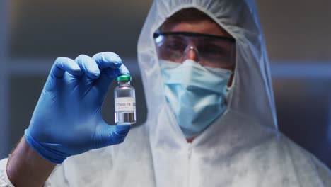 caucasian male medical worker wearing protective clothing mask and gloves holding vaccine vial in la