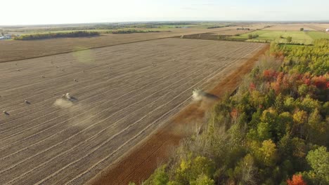 aerial view of a farm combine as it cuts corn stalks and piles chaff for the baling machine following behind gathering the material into large round bales for winter. zoom in, forward motion.
