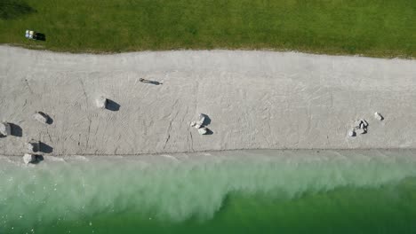 Person-walking-on-white-beach-of-Molveno-Lake,-Trentino-Alto-Adige,-Italy