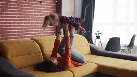 Madre-Levantando-A-La-Niña-En-El-Aire-Sobre-Sus-Tobillos,-Pretendiendo-Volar-En-Casa