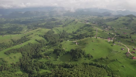 lush green hills with scattered houses, under a cloudy sky, aerial view