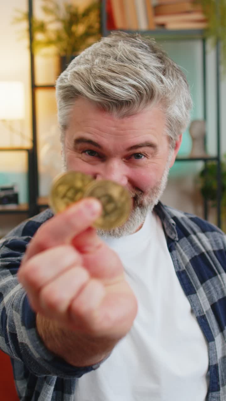 Happy middleaged man successful stock trader holds covering eyes with golden bitcoins at home room