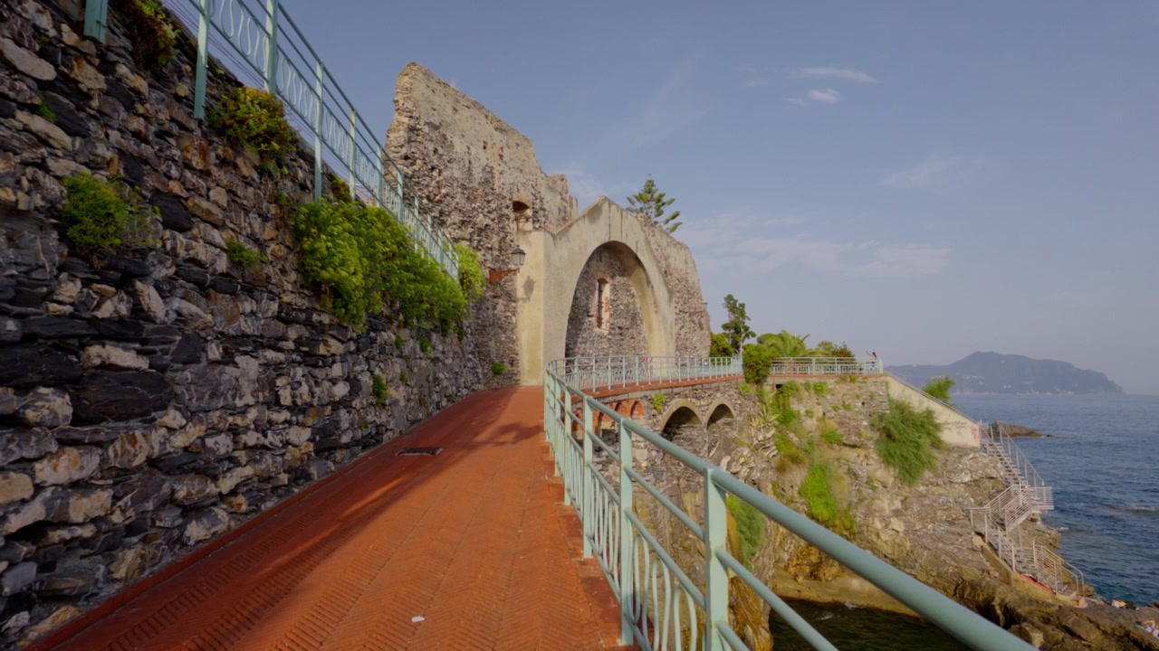Sendero de piedra con arco histórico a lo largo de la rocosa costa de Liguria bajo un cielo despejado.