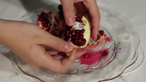 Female-hands-peeling-skin-of-pomegranate-and-gathering-juicy-seeds-for-preparing-a-fruit-salad,-close-up-view